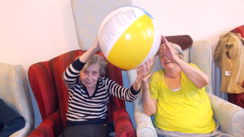 two female care clients enjoying a ball game activity with a larger group around them