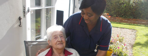 carer outside with resident in large garden by her room door to access garden