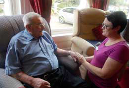 resident in lounge responding to happily to carers assistance and company